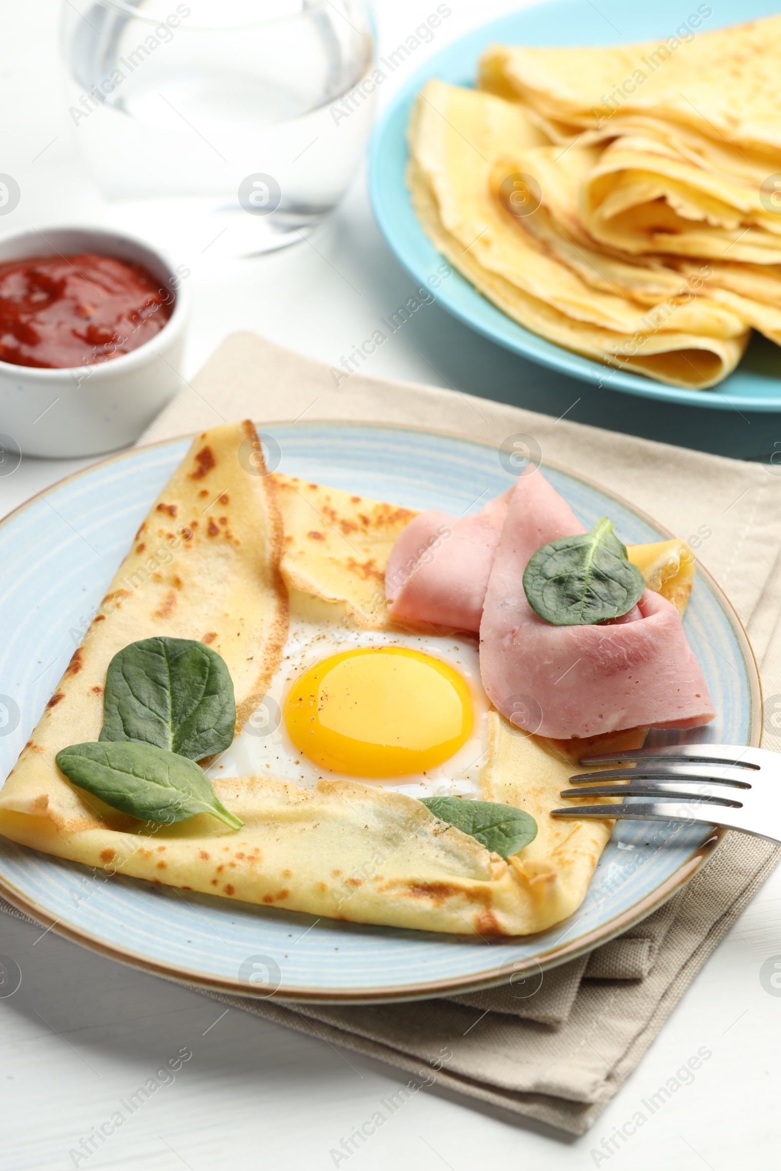 Photo of Delicious crepes with egg, ham, basil and sauce on white wooden table, closeup