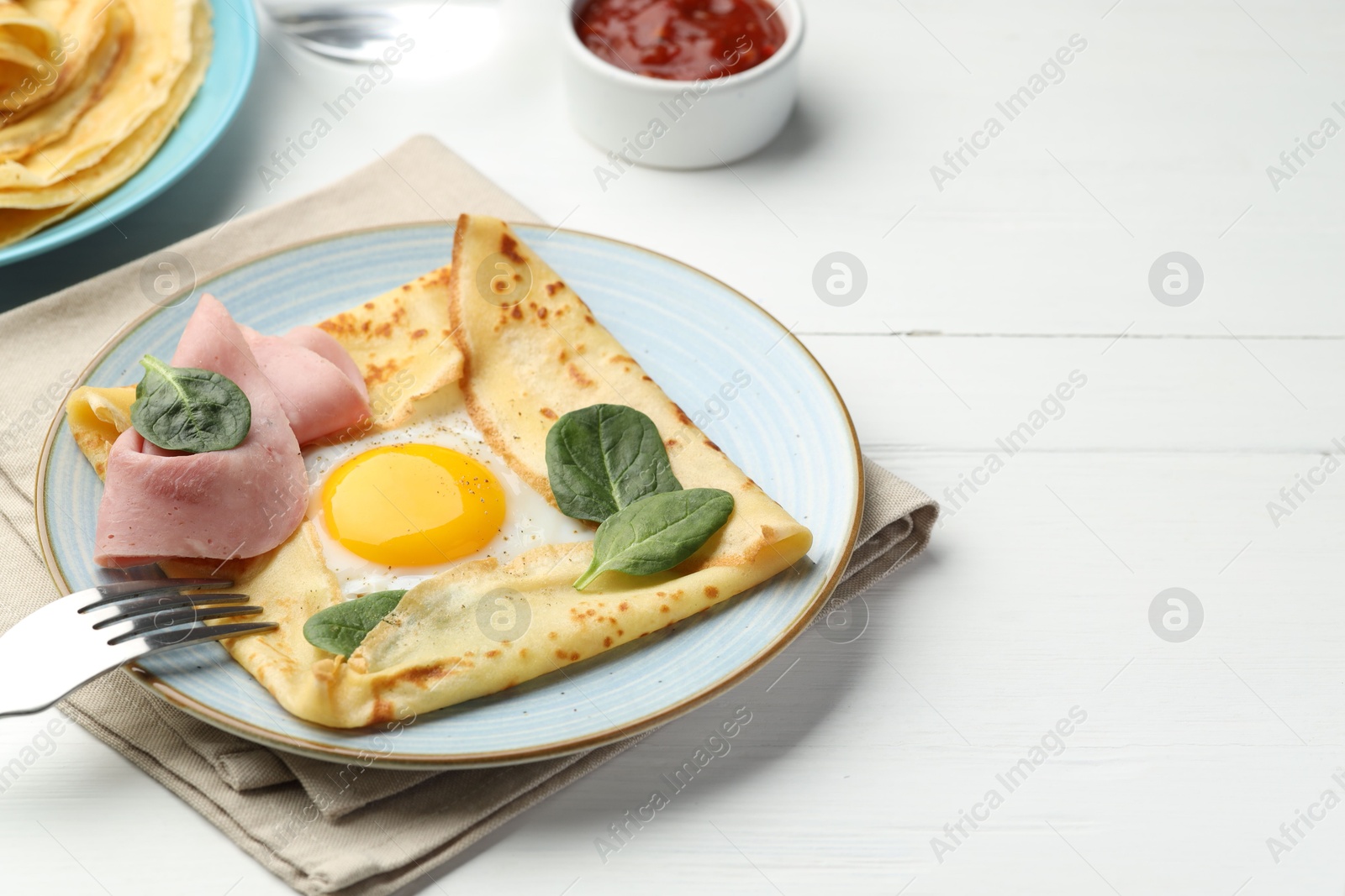 Photo of Delicious crepes with egg, ham, basil and sauce on white wooden table, closeup. Space for text