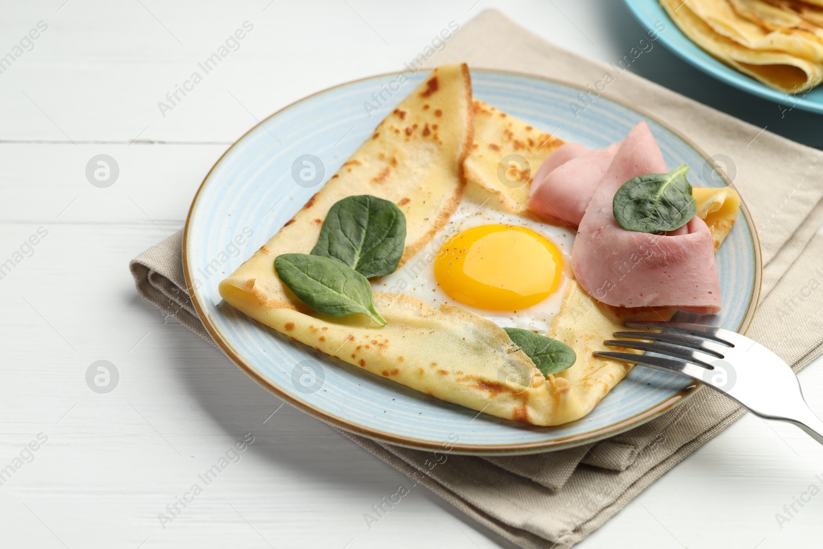 Photo of Delicious crepe with egg, ham and basil on white wooden table, closeup