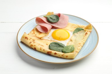 Photo of Delicious crepe with egg, ham and basil on white wooden table, closeup