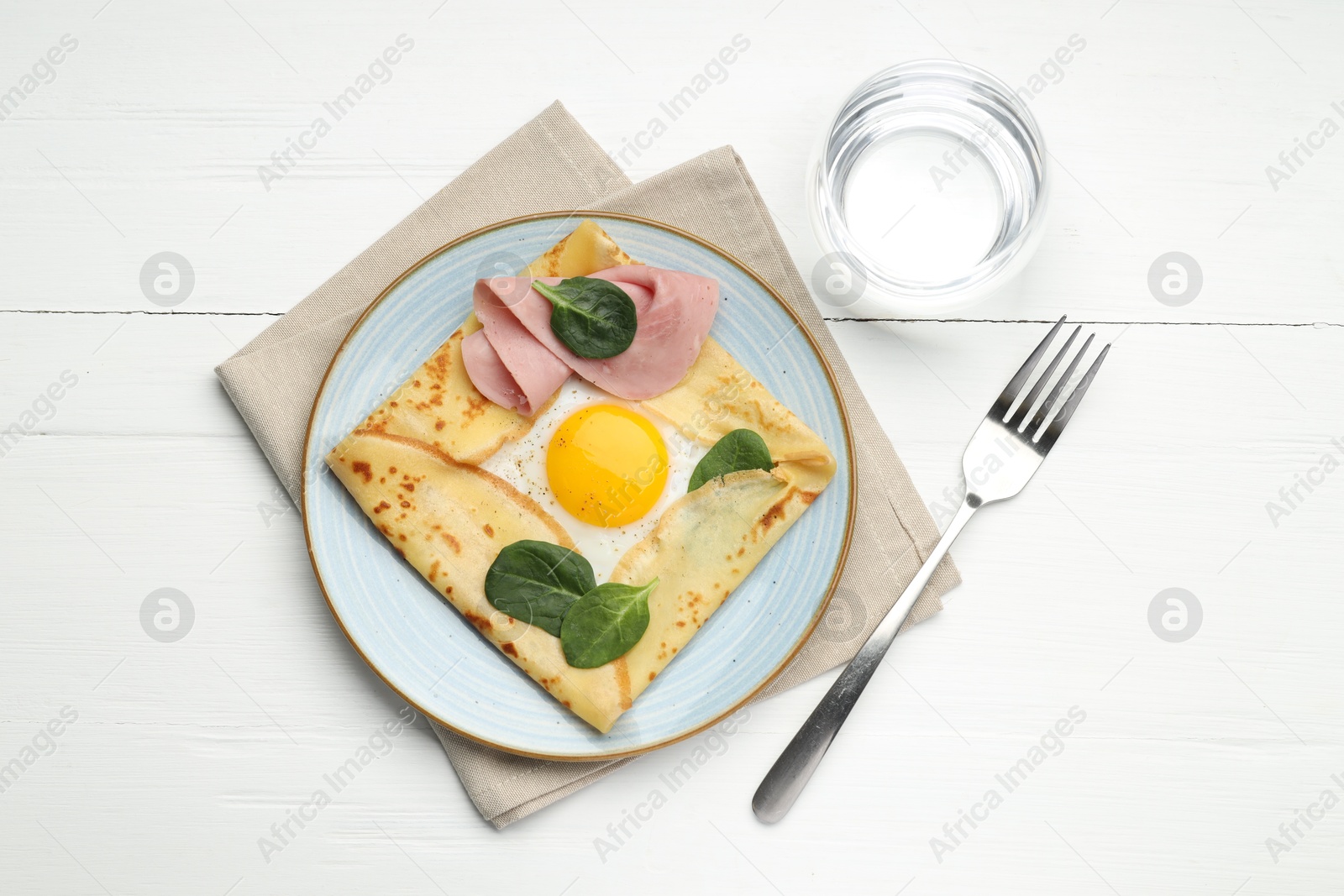 Photo of Delicious crepe with egg, ham, basil and water on white wooden table, flat lay