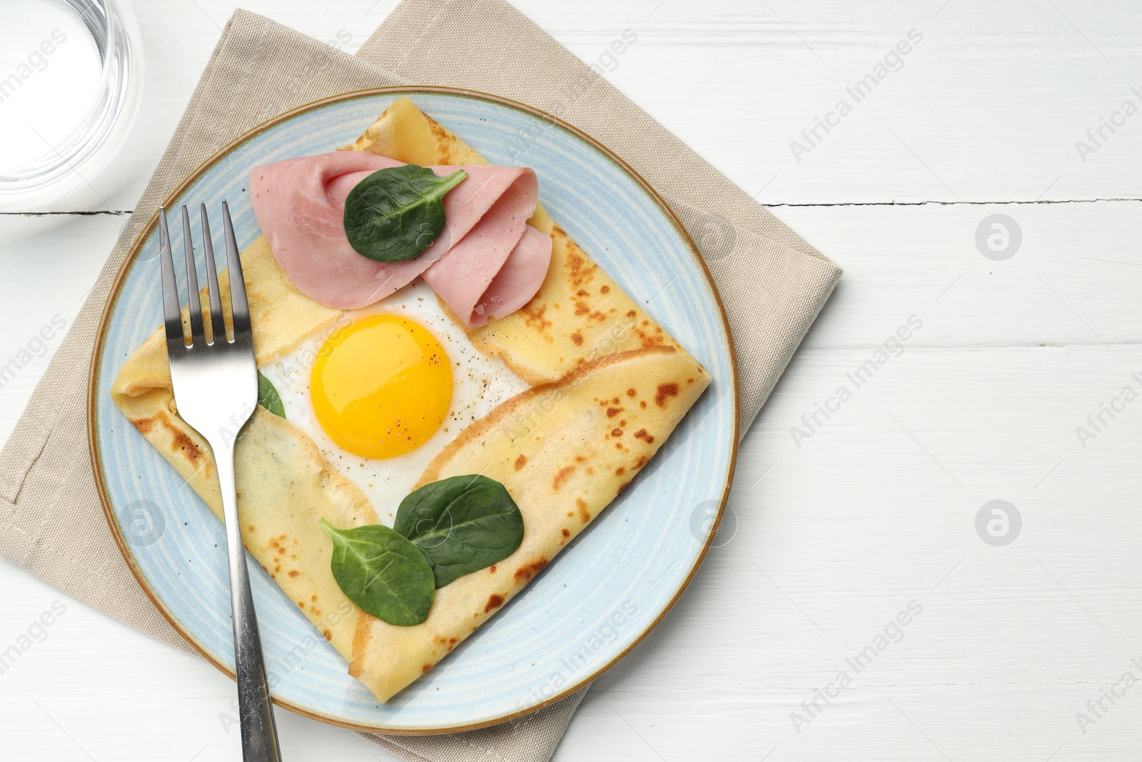 Photo of Delicious crepe with egg, ham, basil and water on white wooden table, flat lay. Space for text