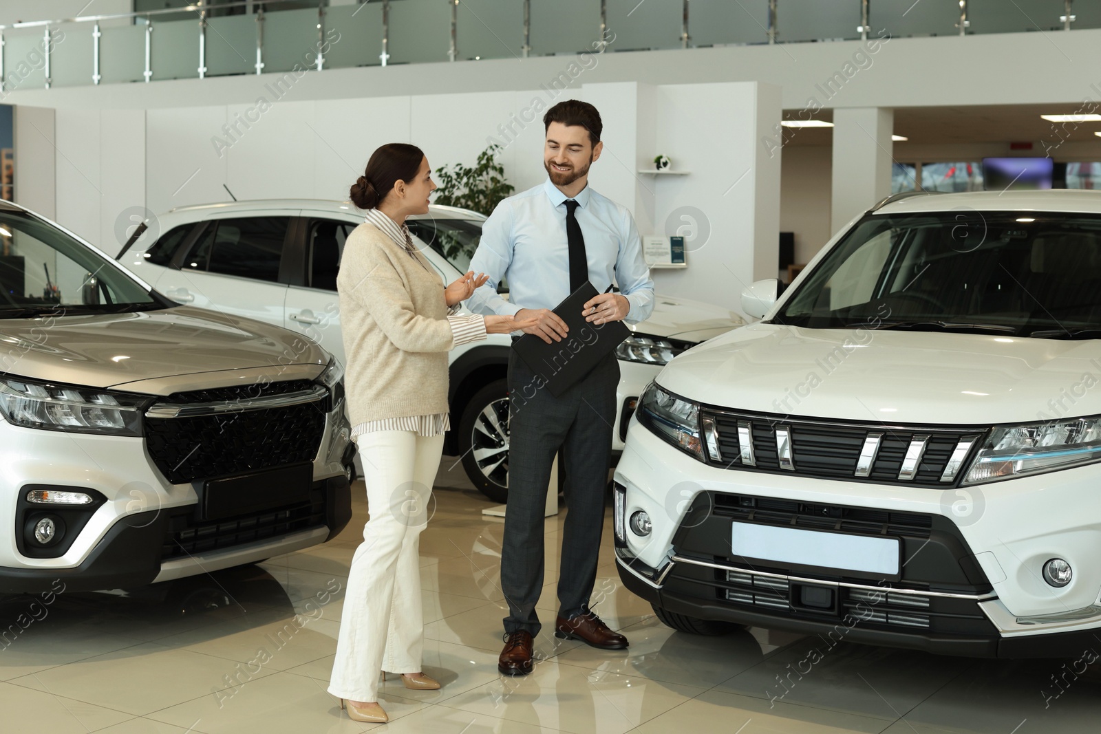 Photo of Happy salesman and client near new car in salon