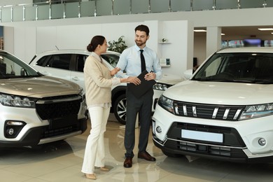 Happy salesman and client near new car in salon