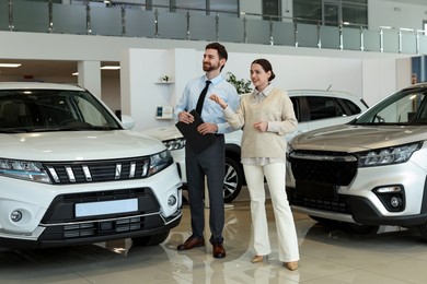 Photo of Happy salesman and client near new car in salon