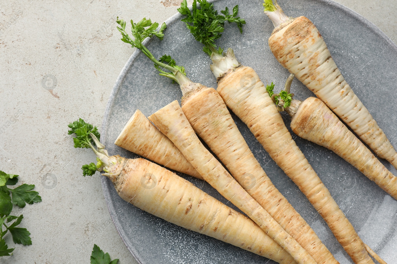 Photo of Fresh parsley and roots on grey table, top view