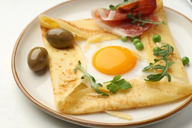 Photo of Delicious crepe with egg, bacon, olives and arugula on white table, closeup