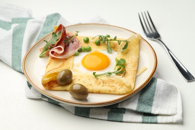 Photo of Delicious crepe with egg, bacon, olives and arugula on white table, closeup