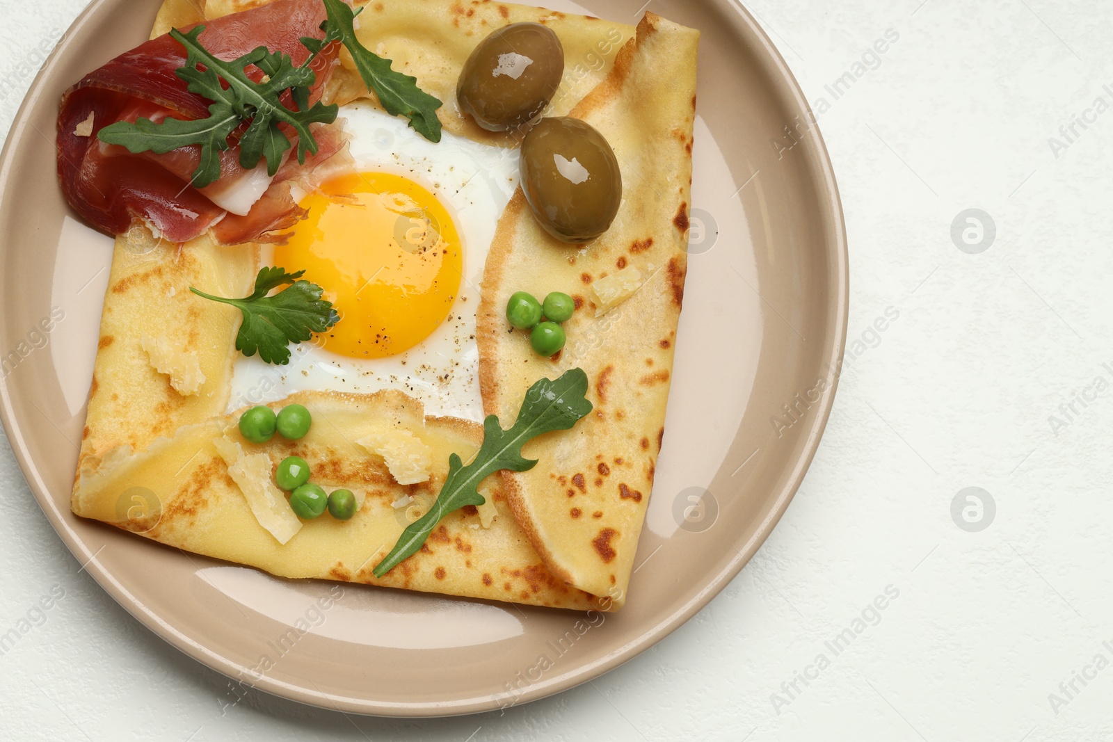 Photo of Delicious crepe with egg, bacon, olives and arugula on white table, top view. Space for text