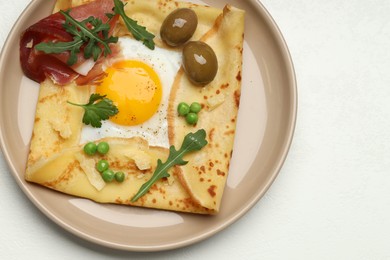 Photo of Delicious crepe with egg, bacon, olives and arugula on white table, top view. Space for text