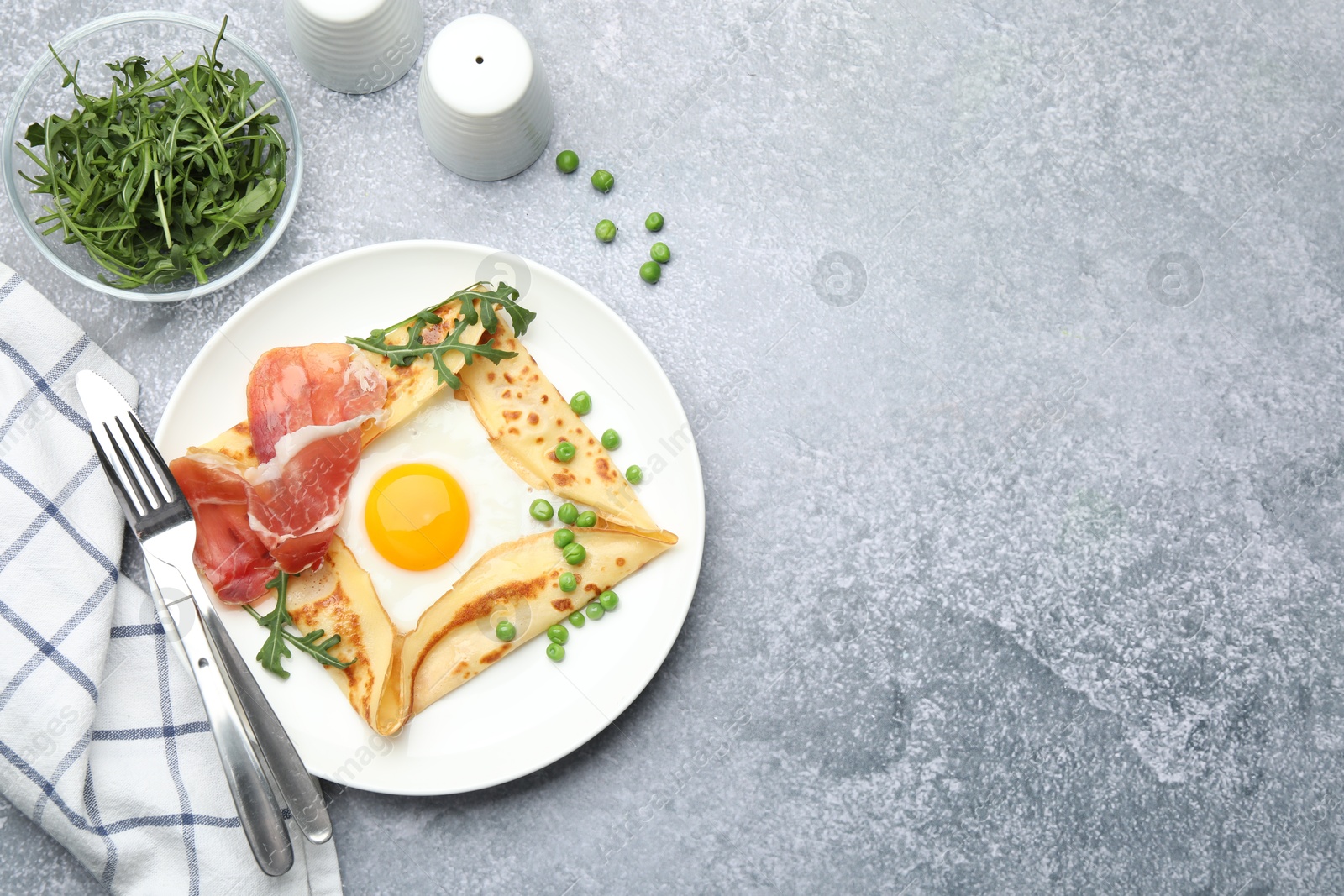 Photo of Delicious crepe with egg, bacon, arugula and green peas on grey table, flat lay. Space for text