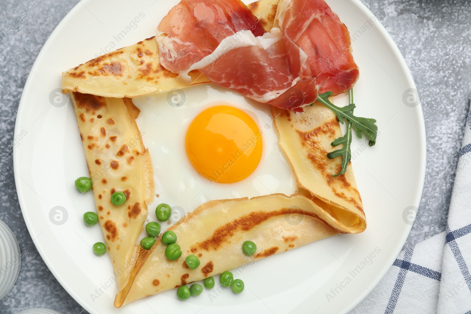 Photo of Delicious crepe with egg, bacon, arugula and green peas on grey table, top view