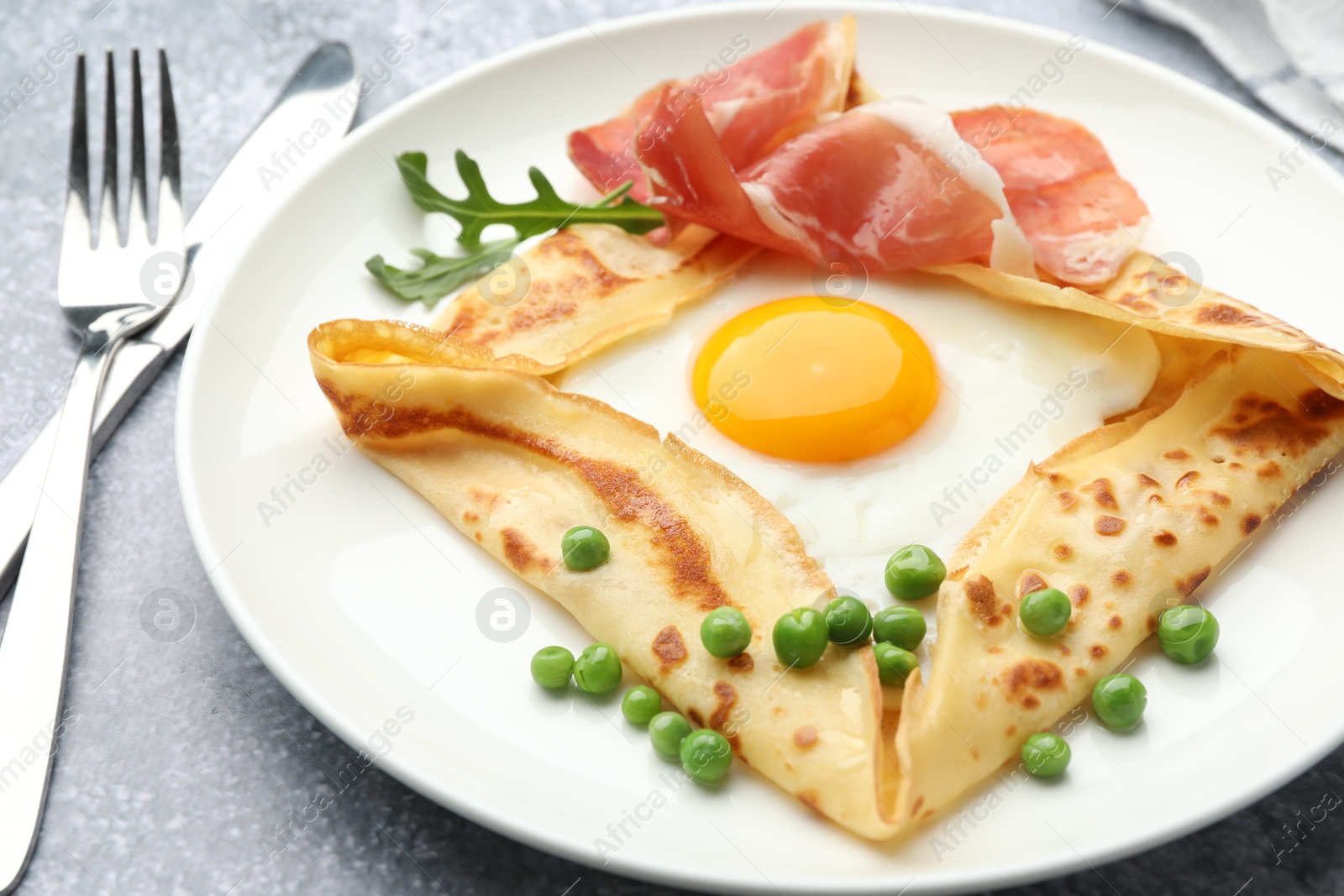 Photo of Delicious crepe with egg, bacon, arugula and green peas on grey table, closeup