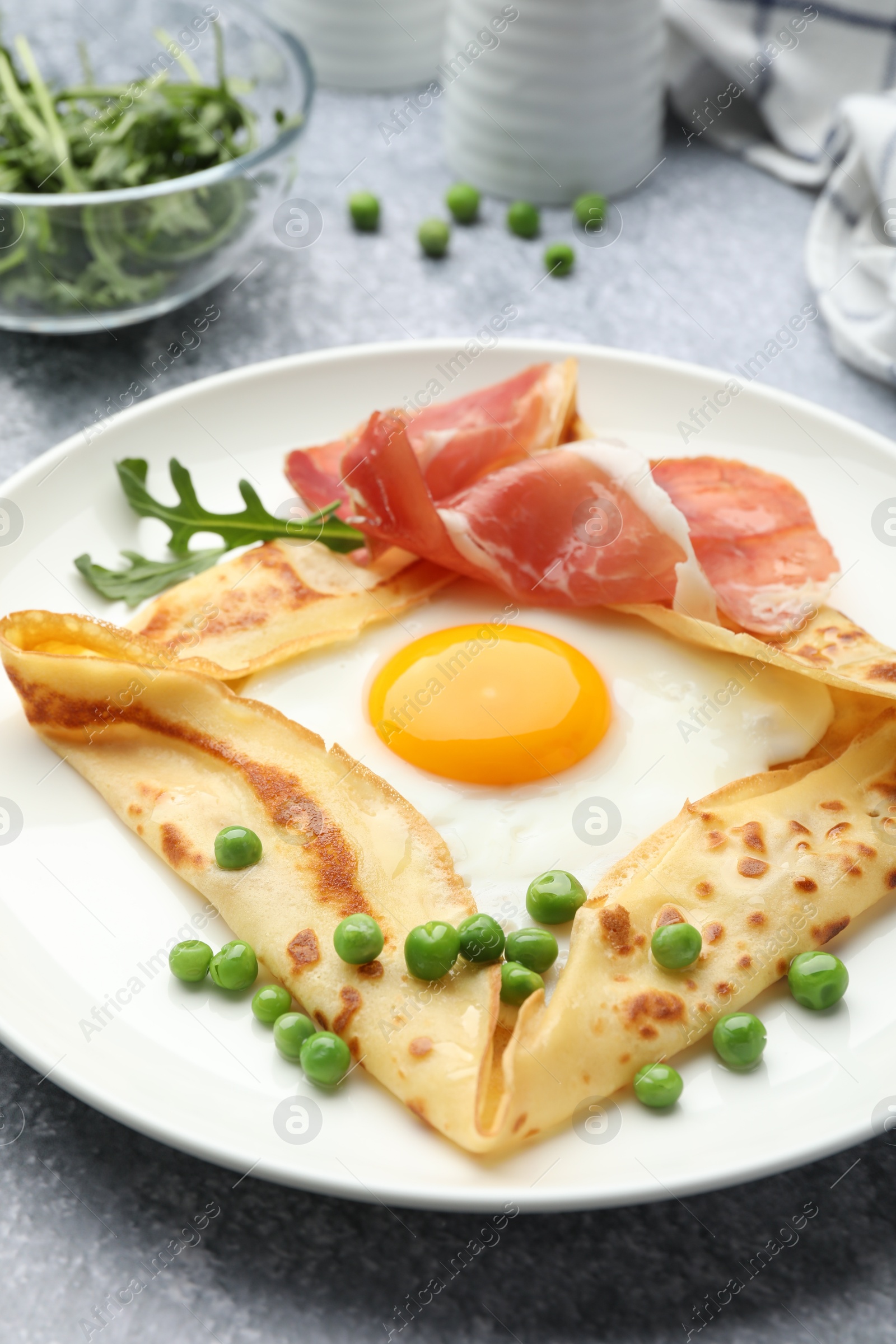 Photo of Delicious crepe with egg, bacon, arugula and green peas on grey table, closeup