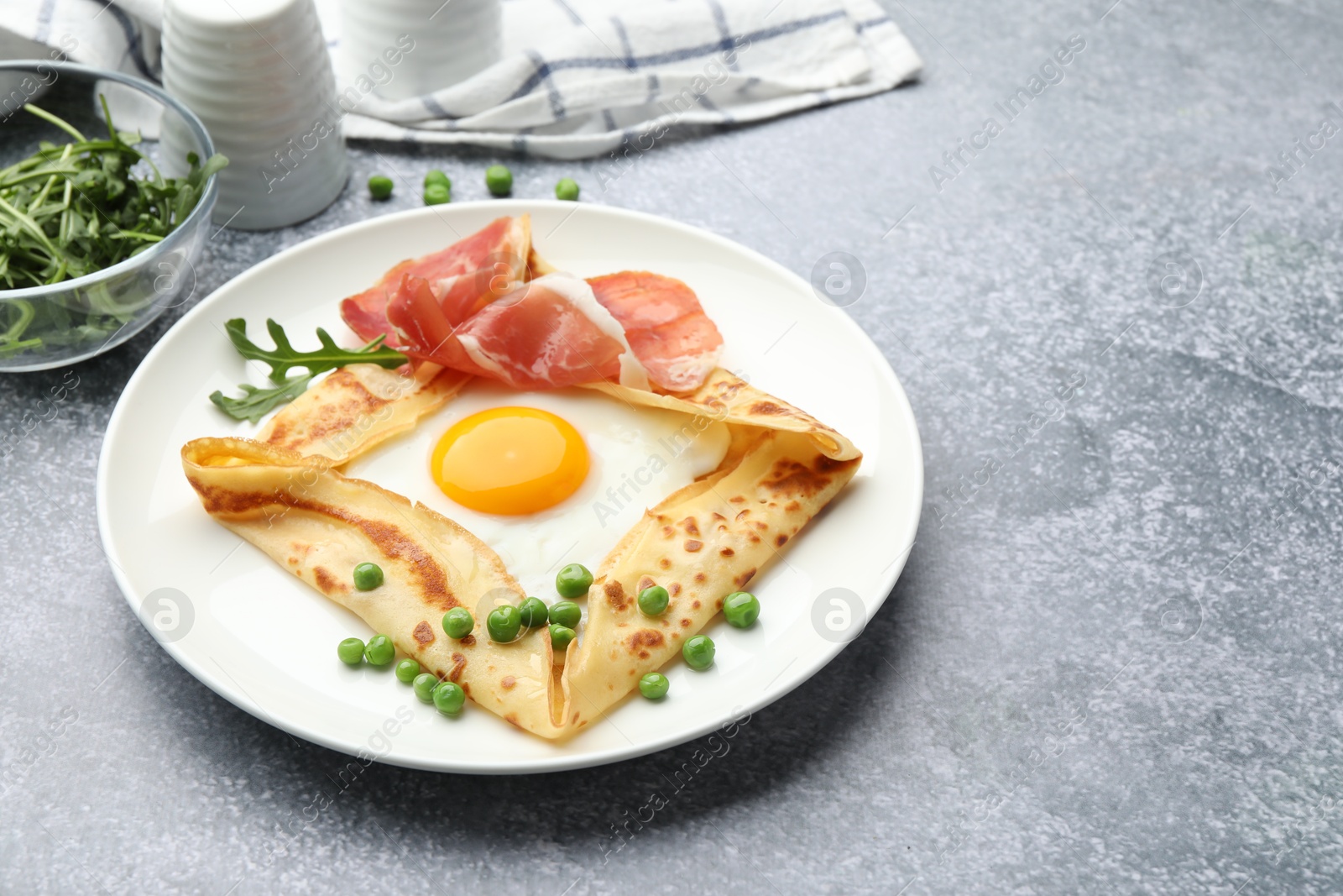 Photo of Delicious crepe with egg, bacon, arugula and green peas on grey table, closeup. Space for text