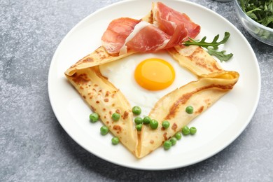 Photo of Delicious crepe with egg, bacon, arugula and green peas on grey table, closeup