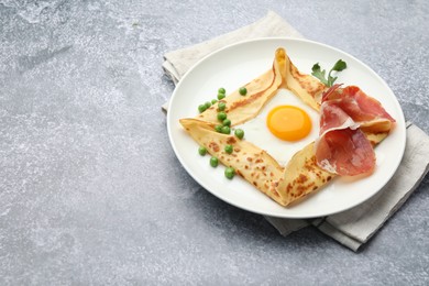 Photo of Delicious crepe with egg, bacon, arugula and green peas on grey table, space for text