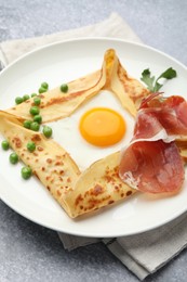 Photo of Delicious crepe with egg, bacon, arugula and green peas on grey table, closeup