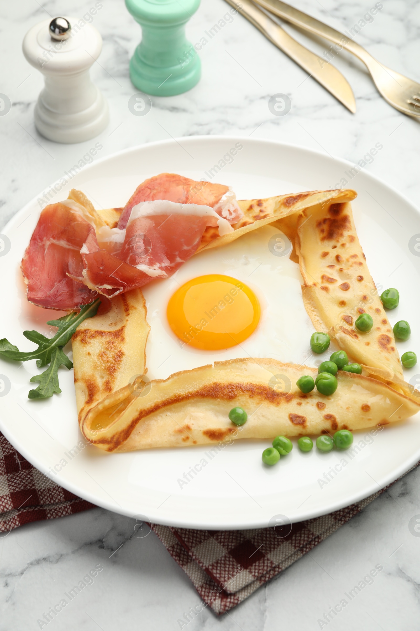 Photo of Delicious crepe with egg, bacon, arugula and green peas on white marble table, closeup