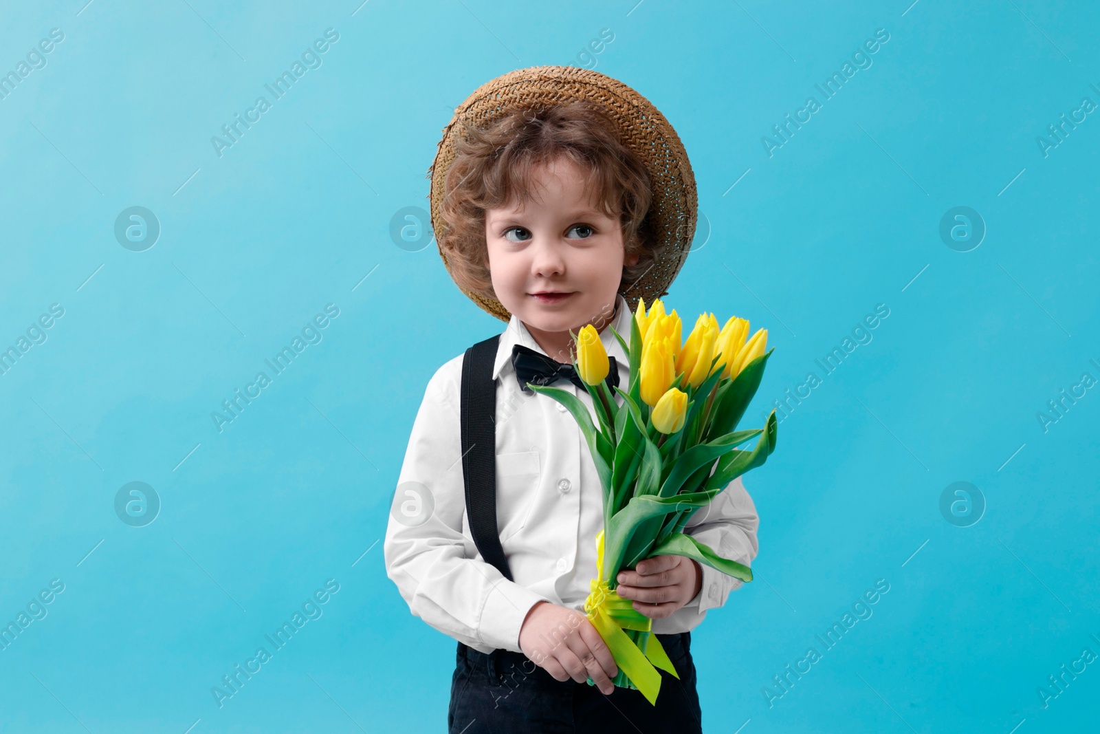 Photo of Cute little boy in wicker hat with bouquet of tulips on light blue background