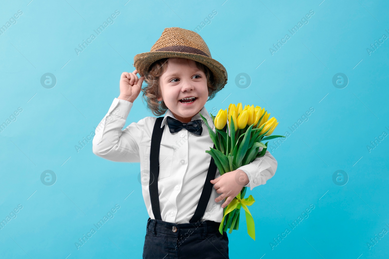 Photo of Cute little boy in wicker hat with bouquet of tulips on light blue background