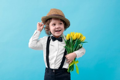 Photo of Cute little boy in wicker hat with bouquet of tulips on light blue background