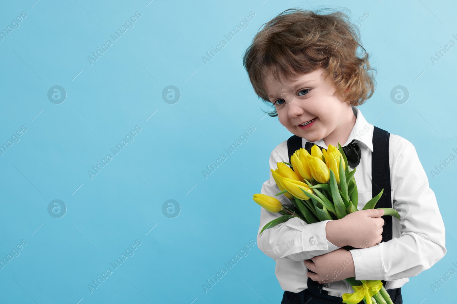 Photo of Cute little boy with bouquet of tulips on light blue background. Space for text