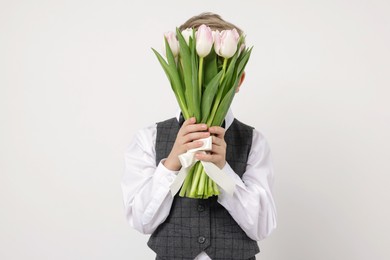 Little boy hiding behind bouquet of tulips on white background