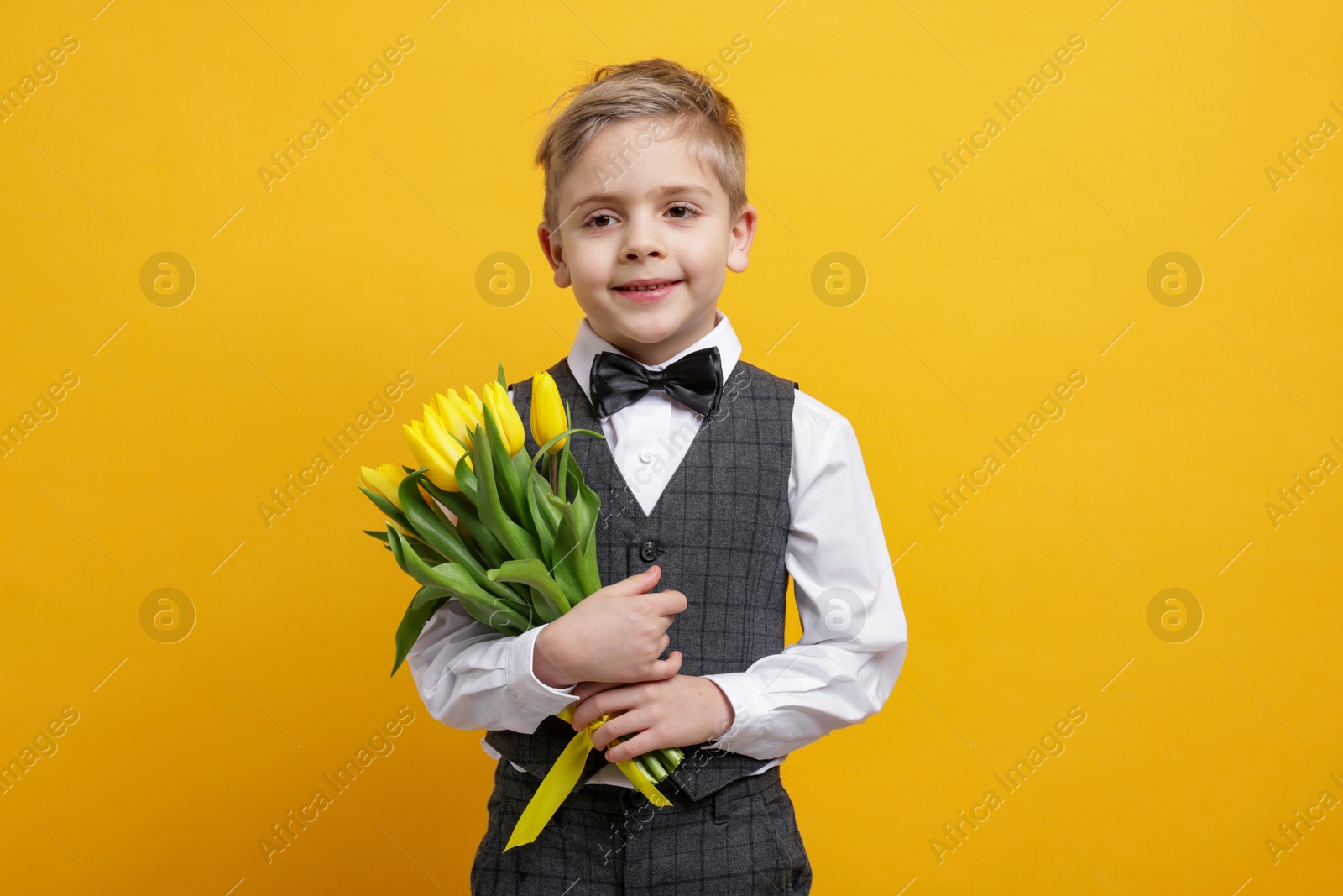 Photo of Cute little boy with bouquet of tulips on yellow background