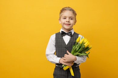 Photo of Cute little boy with bouquet of tulips on yellow background. Space for text