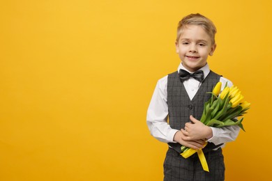 Photo of Cute little boy with bouquet of tulips on yellow background. Space for text