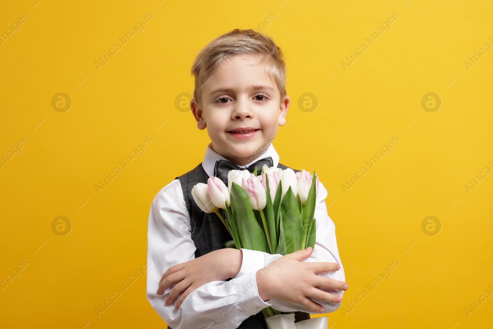 Photo of Cute little boy with bouquet of tulips on yellow background