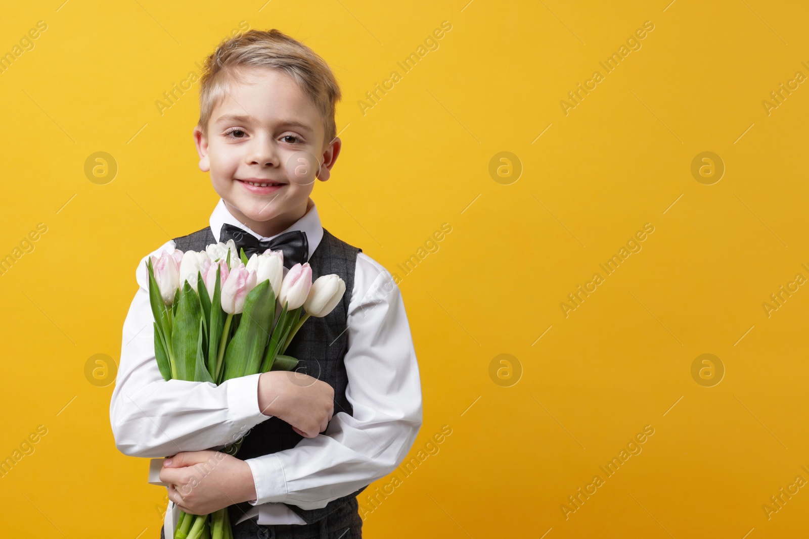 Photo of Cute little boy with bouquet of tulips on yellow background. Space for text