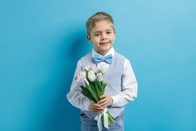 Photo of Cute little boy with bouquet of tulips on light blue background