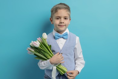 Photo of Cute little boy with bouquet of tulips on light blue background