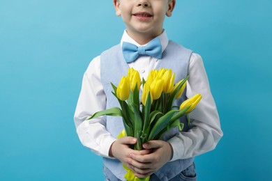 Photo of Little boy with bouquet of tulips on light blue background, closeup