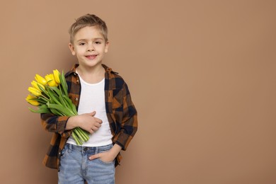 Photo of Cute little boy with bouquet of tulips on brown background. Space for text