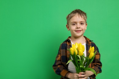 Photo of Cute little boy with bouquet of tulips on green background. Space for text