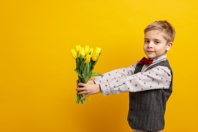 Photo of Cute little boy with bouquet of tulips on yellow background. Space for text