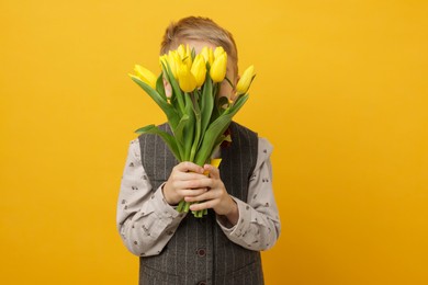 Photo of Little boy hiding behind bouquet of tulips on yellow background