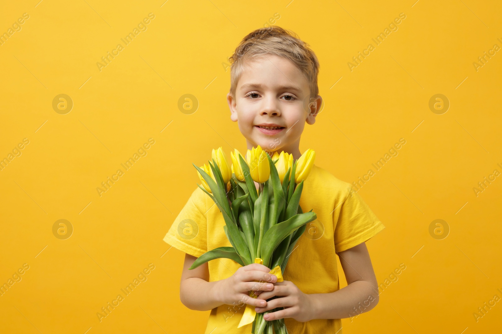 Photo of Cute little boy with bouquet of tulips on yellow background