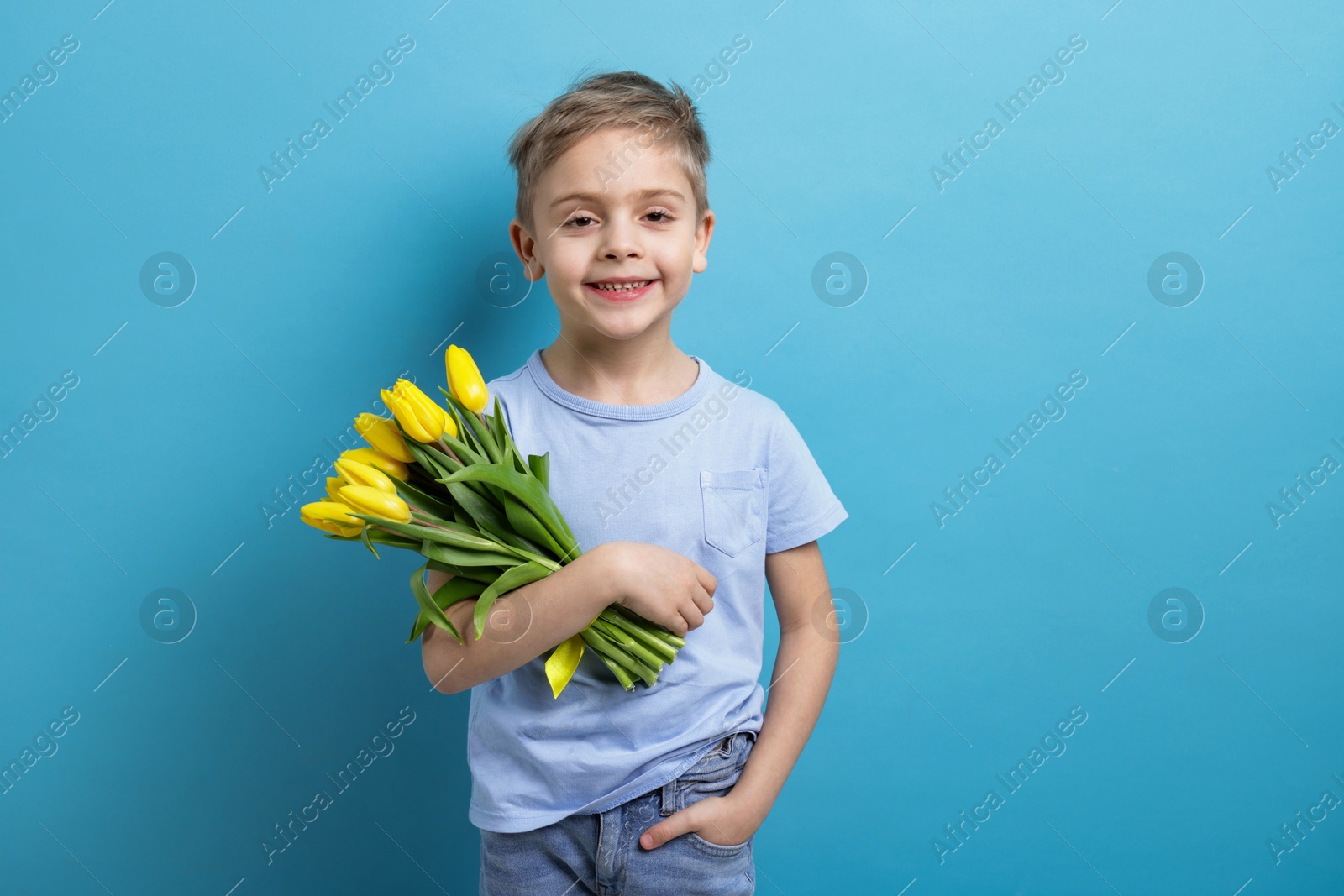 Photo of Cute little boy with bouquet of tulips on light blue background