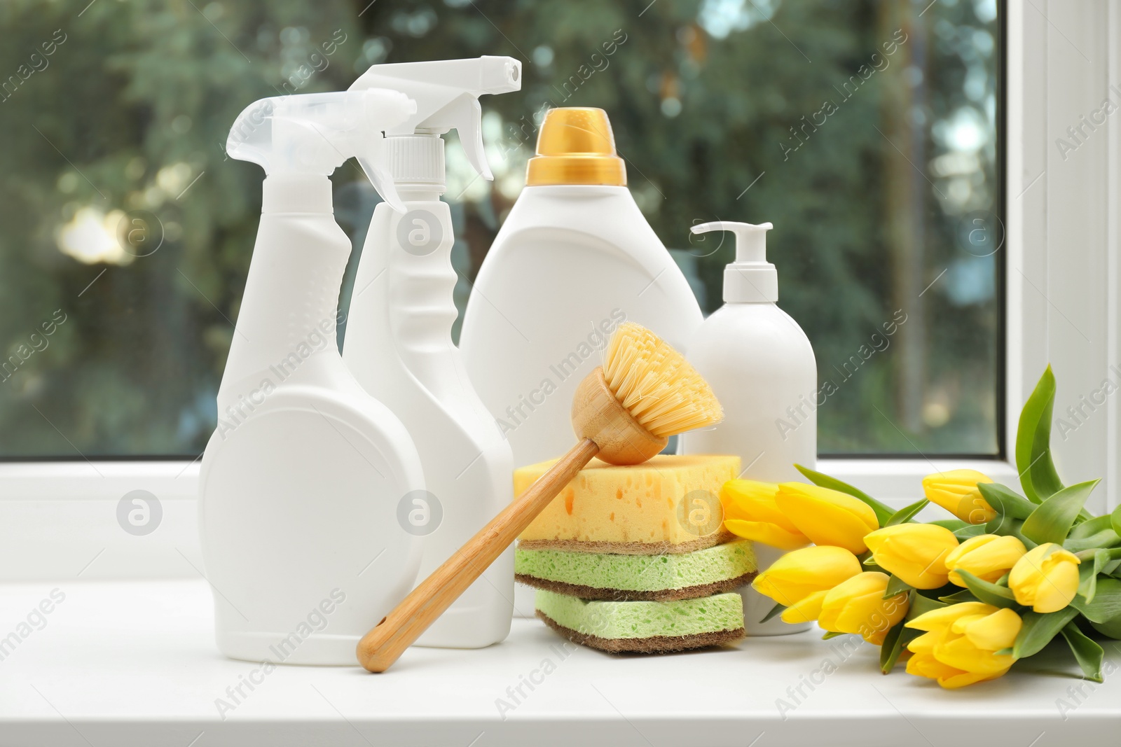 Photo of Spring cleaning. Detergents, supplies and tulips on windowsill indoors