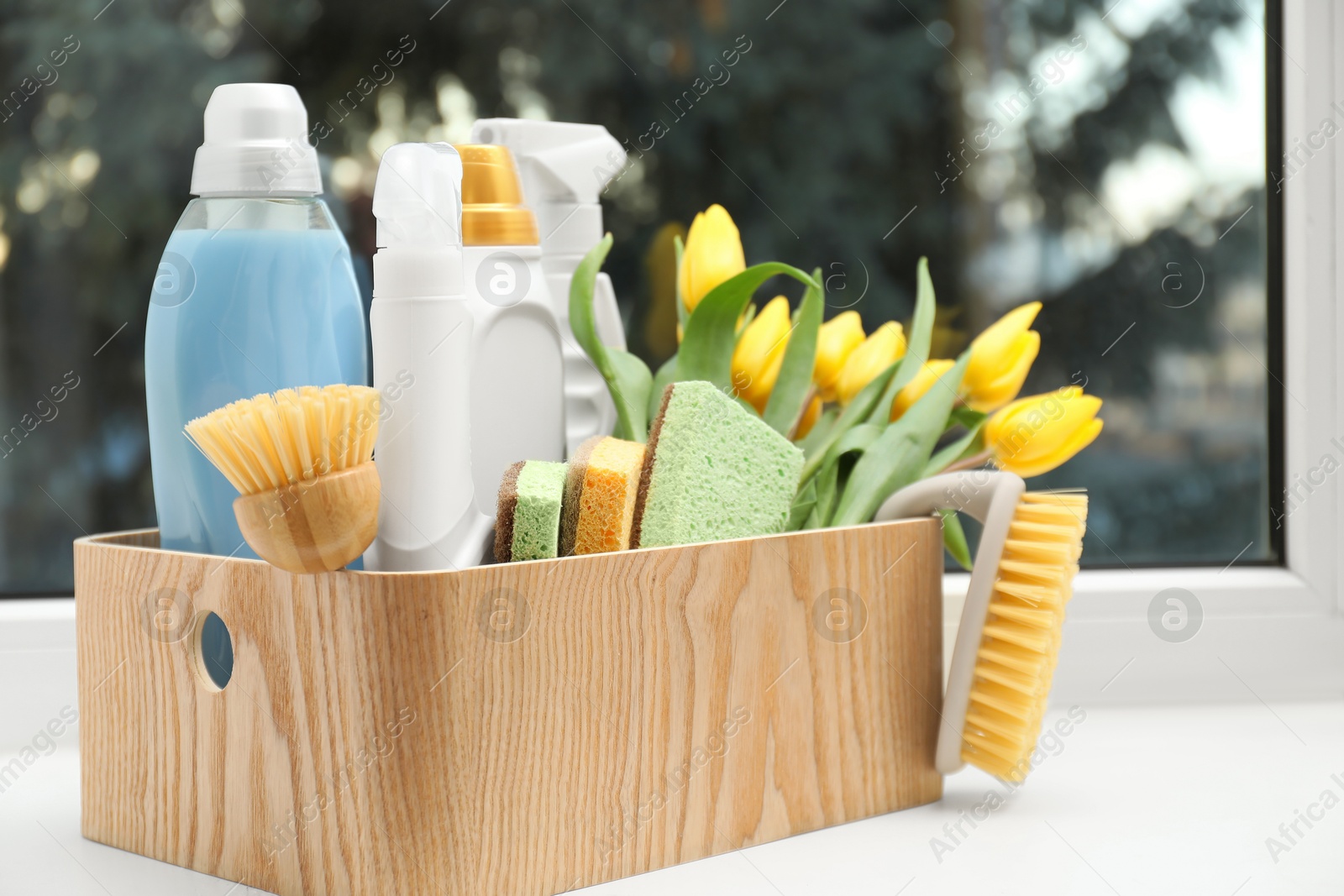 Photo of Spring cleaning. Detergents, supplies and tulips on windowsill indoors