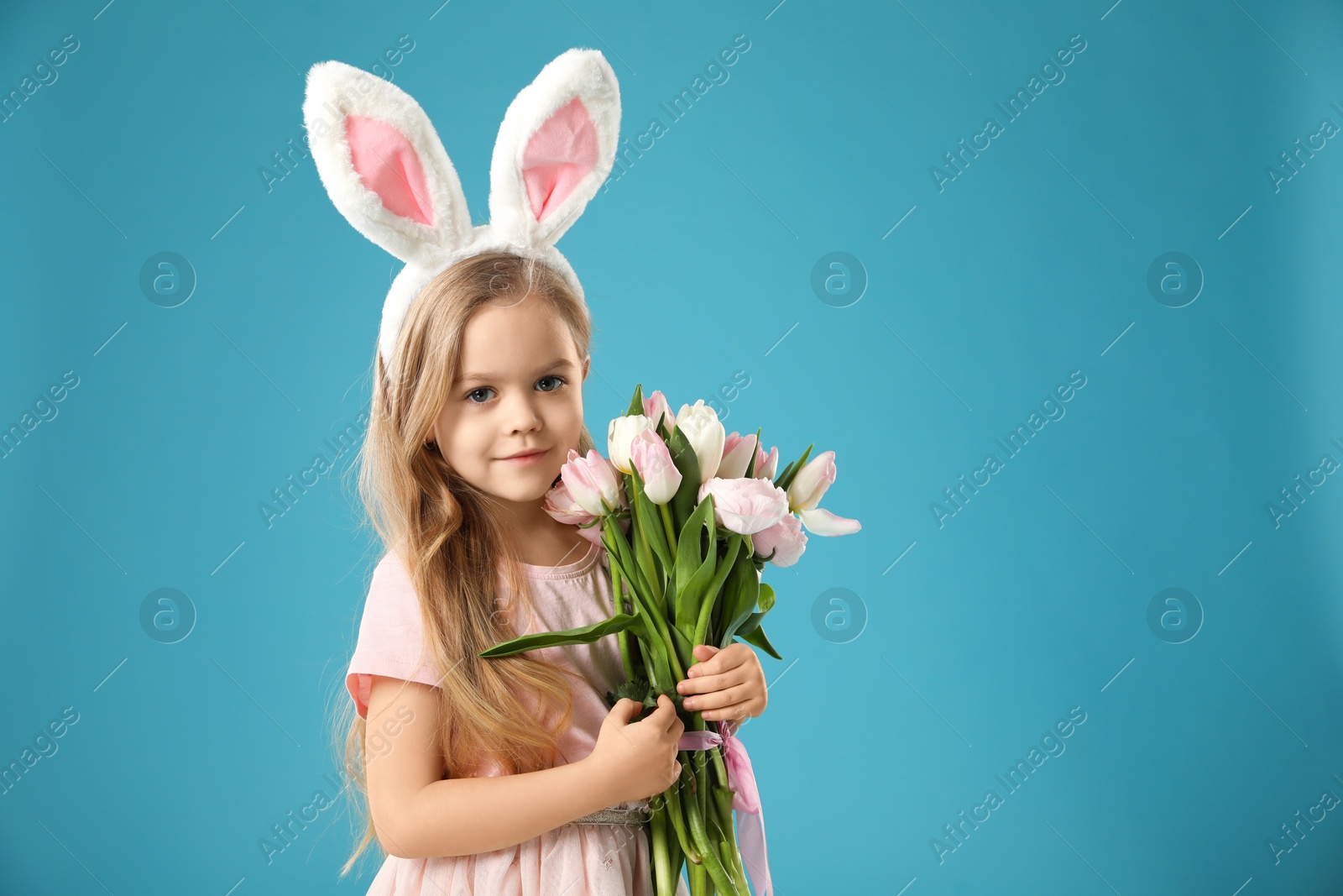 Photo of Cute little girl with bunny ears and spring flowers on light blue background. Easter celebration