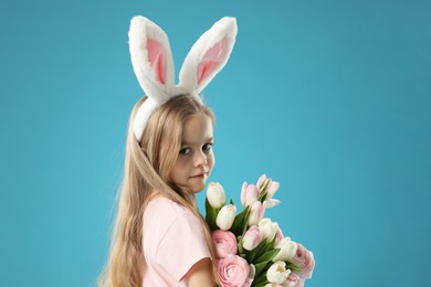 Photo of Cute little girl with bunny ears and spring flowers on light blue background. Easter celebration