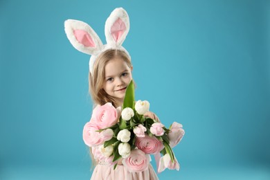 Cute little girl with bunny ears and spring flowers on light blue background. Easter celebration