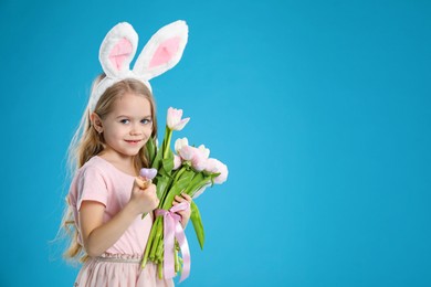 Cute little girl with bunny ears and spring flowers on light blue background, space for text. Easter celebration