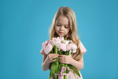 Cute little girl with bouquet of beautiful spring flowers on light blue background