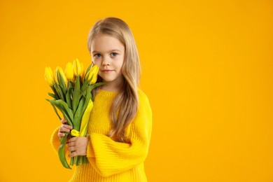 Photo of Cute little girl with beautiful yellow tulips on orange background, space for text. Spring season